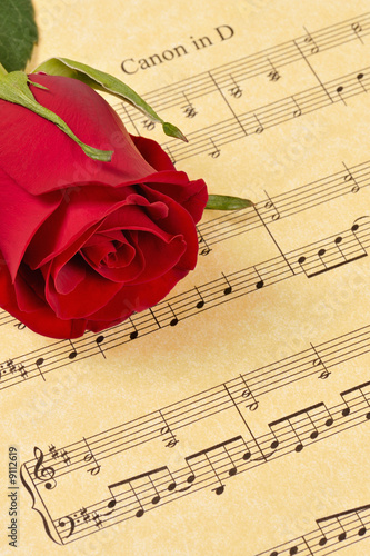 A red rose bud rests on parchment paper sheet music.