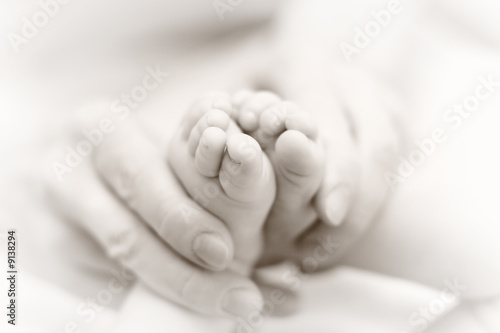 Mother gently massage baby legs. Slightly toned B&W image