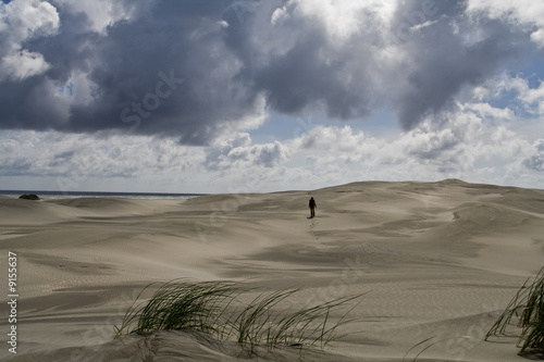 A lonely girl walking over a sand dune