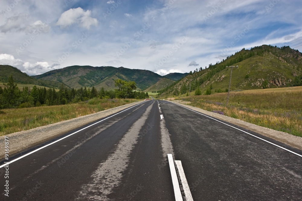 asphalt road among mountains and low cloud sky