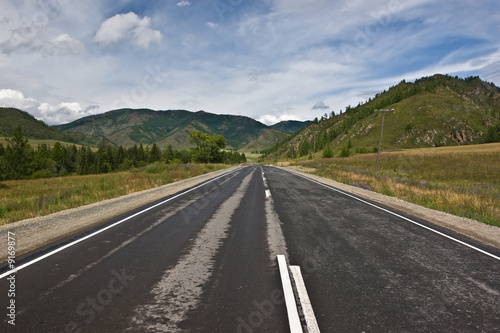 asphalt road among mountains and low cloud sky