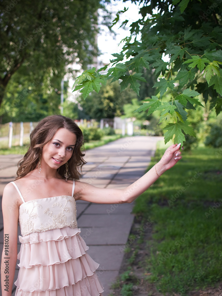 Naklejka premium Girl teenager stands outdoor and touches leaf of maple.