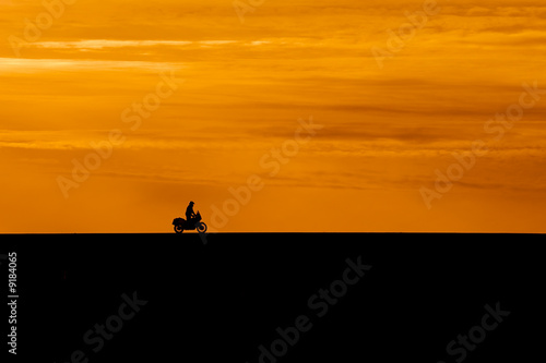 black silhouette of biker on orange sunset sky background