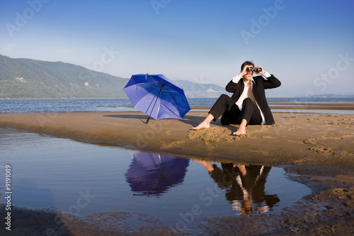 Man sitting on the beach looking through the binocular