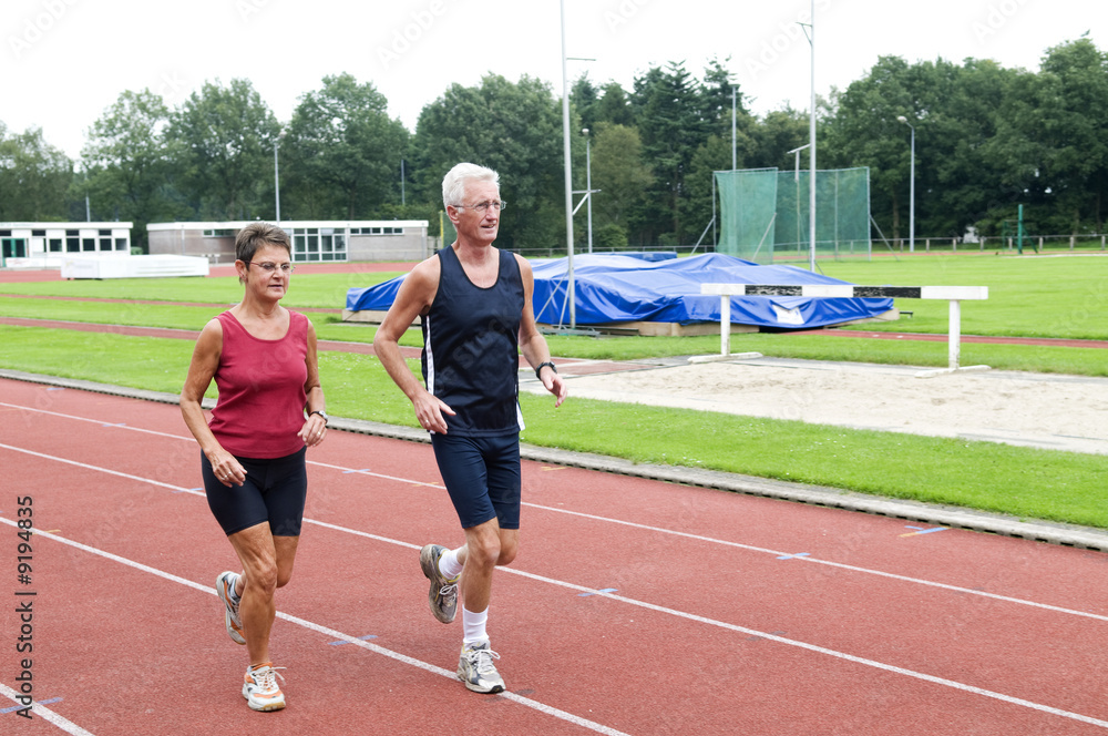 Senior couple running together on a track in a stadium.