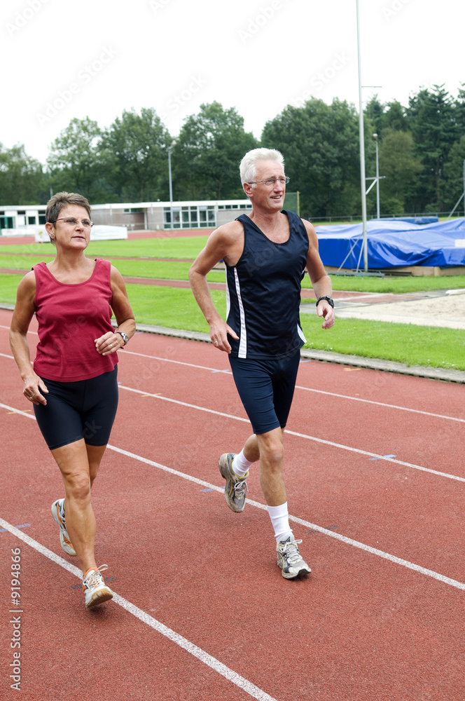 Senior couple running together on a track in a stadium.