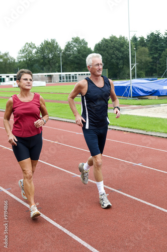 Senior couple running together on a track in a stadium.