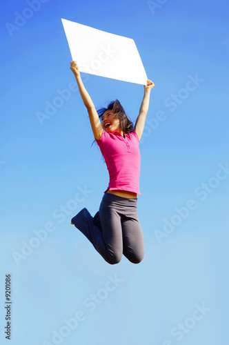 Girl jumping with sign in front of a big blue sky.