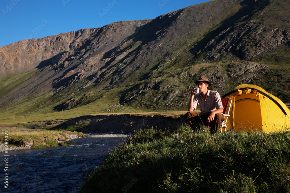 Naklejka premium man is drinking at the camp in mountains near the stream.