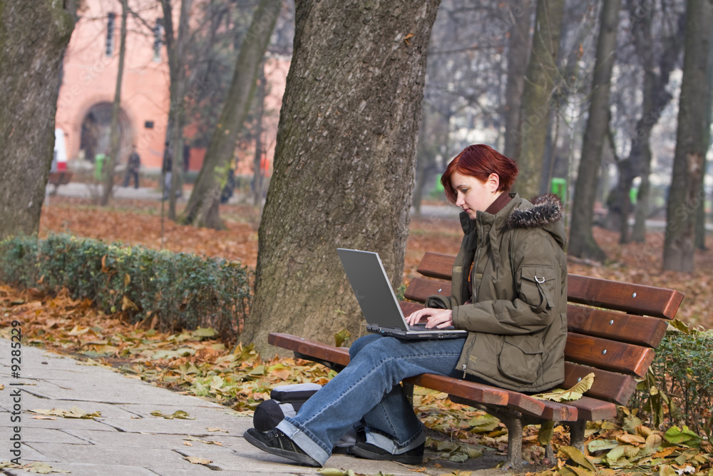 Young woman working on a laptop in a park in autumn. Young woman working on a laptop in a park in autumn.