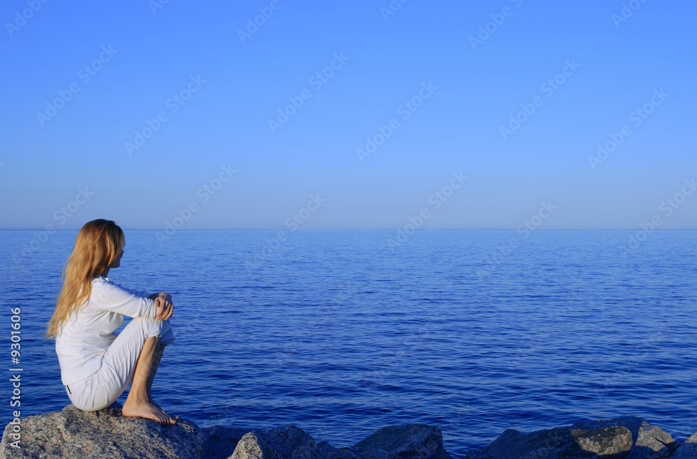 Girl sitting on the rock by the peaceful sea at sunset.