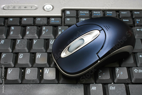 A wireless mouse put on keyboard of a laptop.
