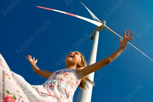 child playing with the wind near a wind turbine
