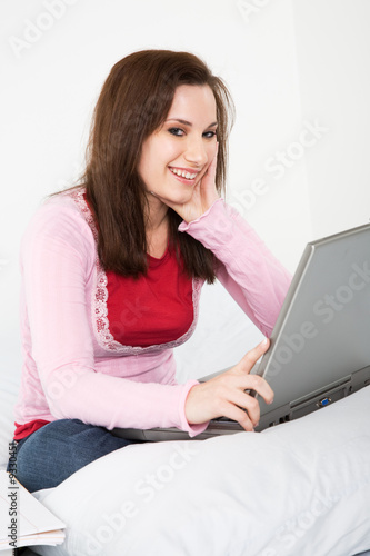 A caucasian female student studying with her laptop on her bed