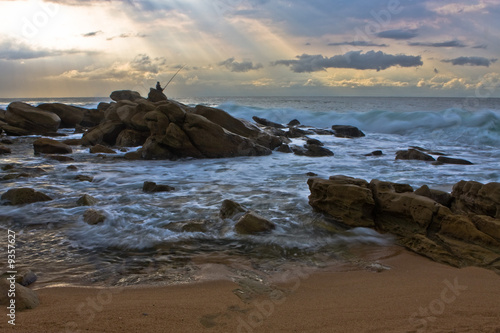 Lone fisherman on the rocks overlooking the deep ocean © Riaan van den Berg