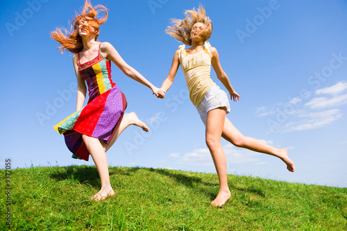 Two happy young women are runing in a field