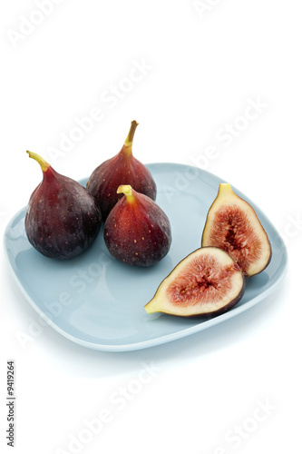 three whole figs and one sliced one on a square blue plate