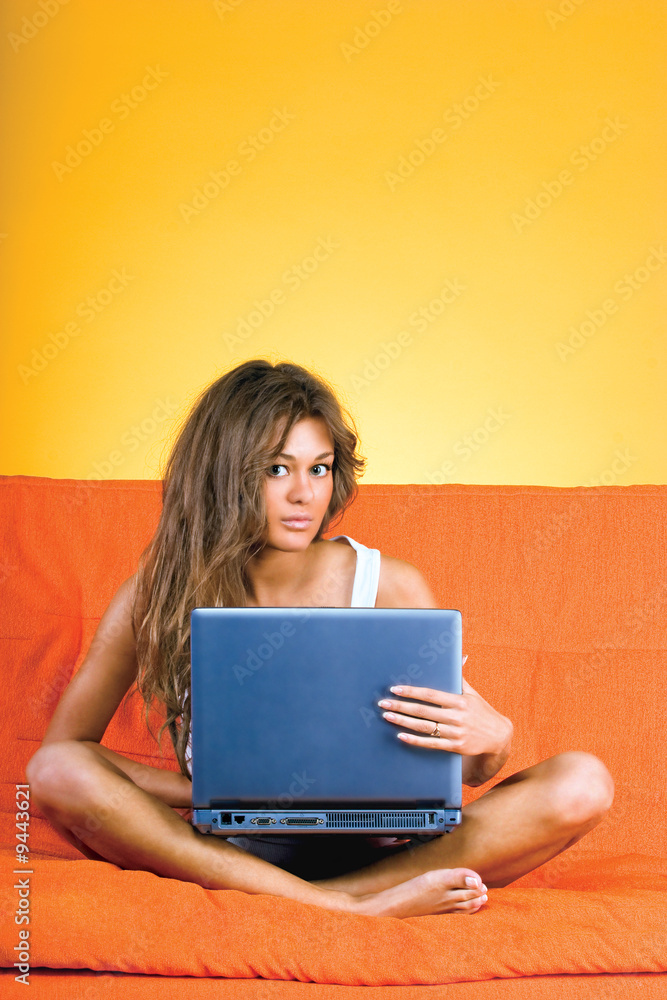 Beautiful young woman sitting on sofa with laptop on her knees Beautiful young woman sitting on sofa with laptop on her knees