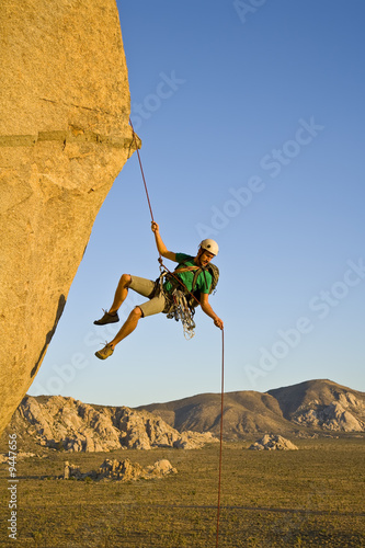 A rock climber rappelling past an overhang.