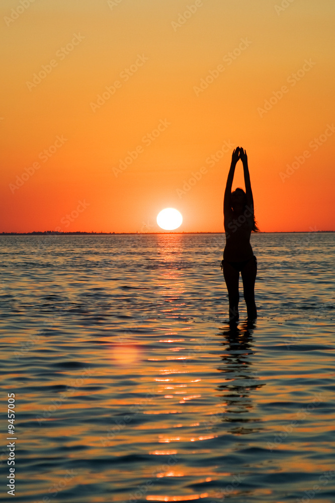 Silhouette of the young woman with hands upwards on a sunset