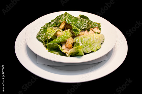 Caesar salad with shrimps on a white plate isolated on black