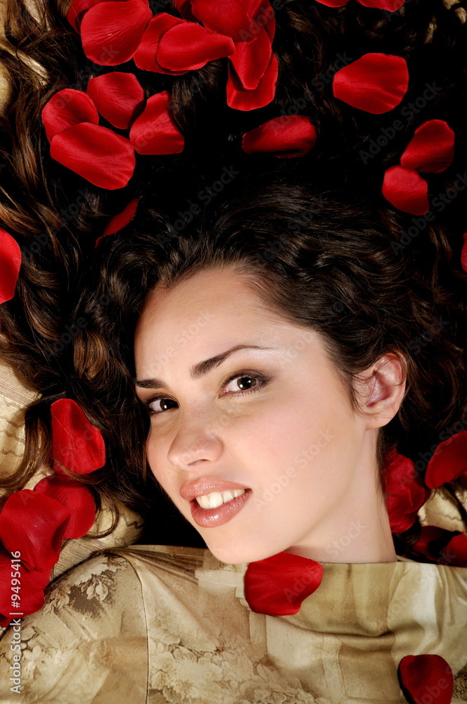 Beautiful woman with red rose petals on golden background Beautiful woman with red rose petals on golden background