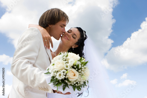 Canvas Print Bride and groom kissing on the blue sky background