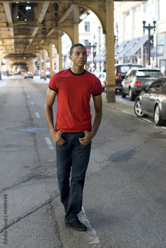 Adult black male with thumbs in jeans walking under El tracks.. Adult black male with thumbs in jeans walking under El tracks..