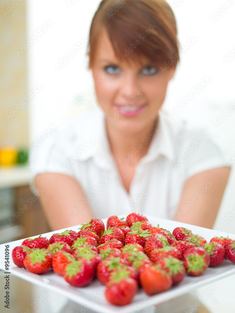 Beautiful woman in kitchen looking at plate with strawberries