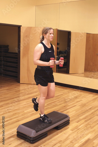 Woman working out in a gym using hand weights and a step. photo