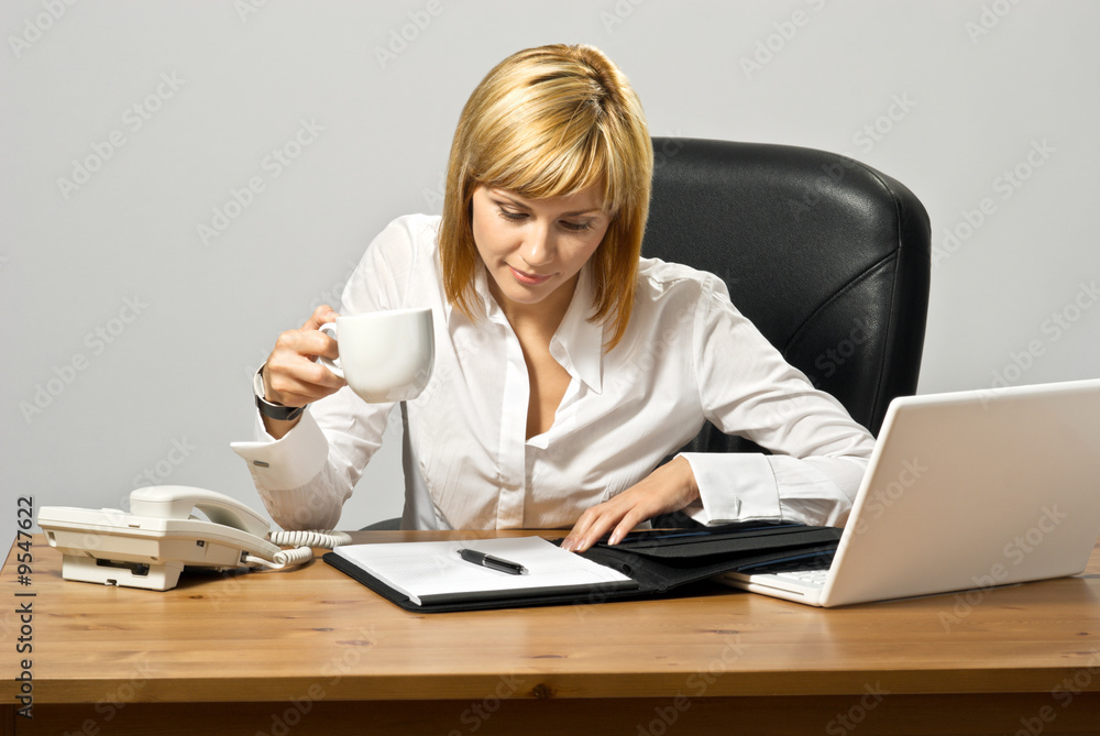 Business lady at a desk reading and drinking coffee. Business lady at a desk reading and drinking coffee.