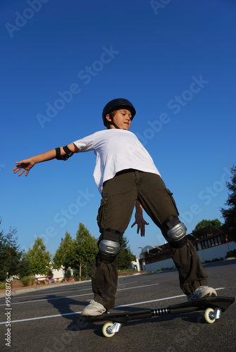 Boy balancing the skateboard shown against the blue sky