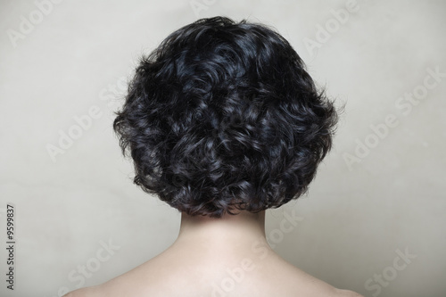 Woman with black curly hair on beige texture background.