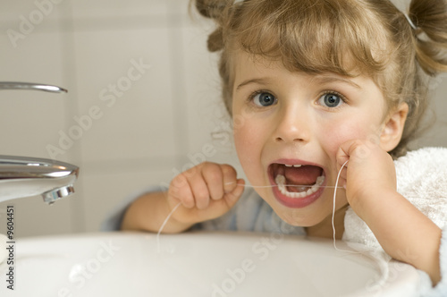 Cute girl cleaning teeth by floss in bathroom