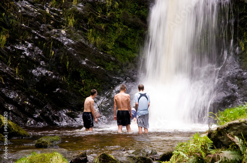 Four young men in a pool under a cold waterfall in Wales