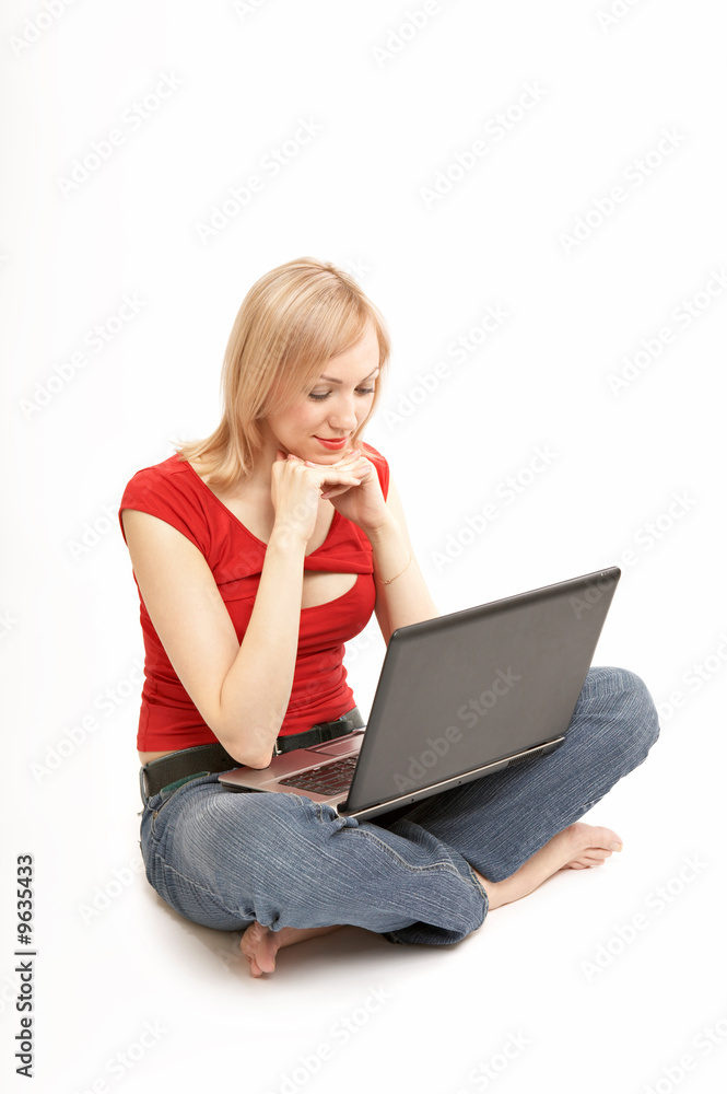 The blonde sits in a cross-legged pose with a laptop isolated The blonde sits in a cross-legged pose with a laptop isolated