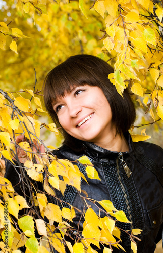 cheerful cute girl in the park looking at yellow leaves