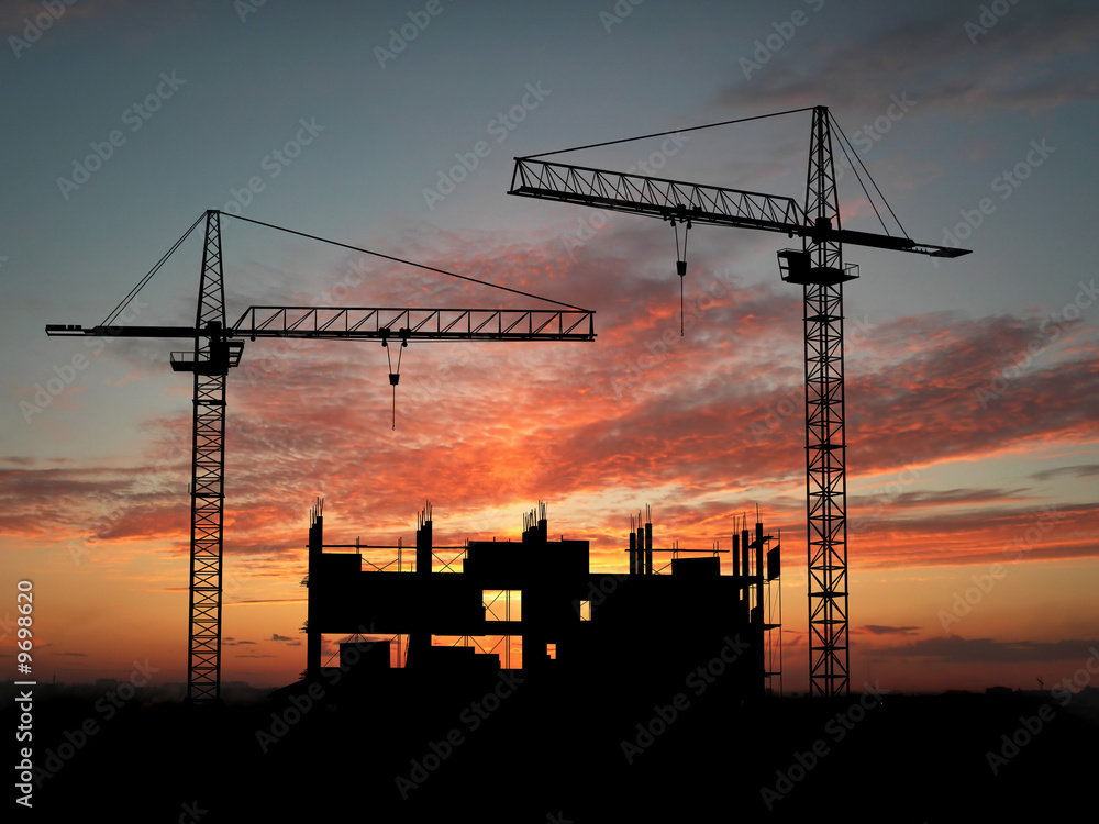 Two cranes build construction over sunset