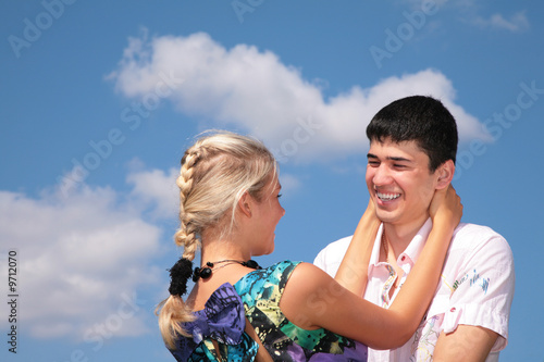 Girl embraces guy for neck on sky background