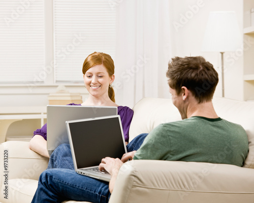 Couple relaxing on sofa in livingroom typing on laptops