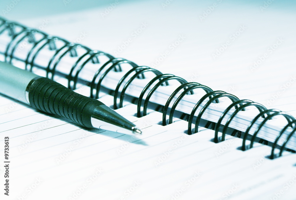 Silver-blue pen lying on opened notebook Silver-blue pen lying on opened notebook