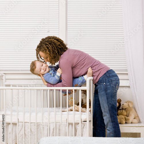 Devoted mother laying son down into crib for nap in bedroom