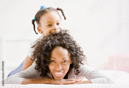 Devoted mother lays on bed with playful daughter photo