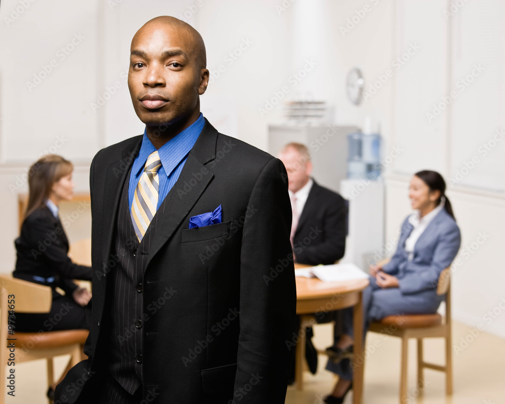 Confident businessman with co-workers in background Confident businessman with co-workers in background