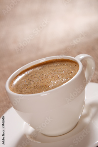 Cup of black coffee with froth on brown background, shallow DOF