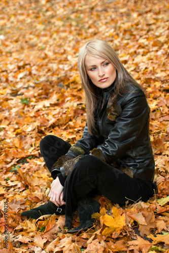 Blond girl sitting in yellow autumn leaves