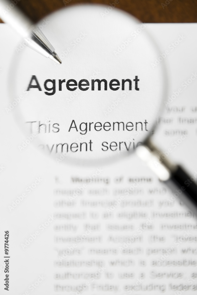 Magnifying glass over agreement paperwork and pen. Magnifying glass over agreement paperwork and pen.