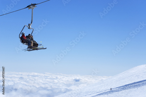 Chair lift with skiers at ski resort above the clouds