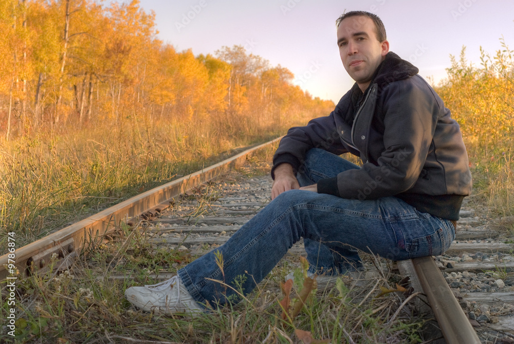 A man sitting on a set of railroad tracks, smiling at the camera