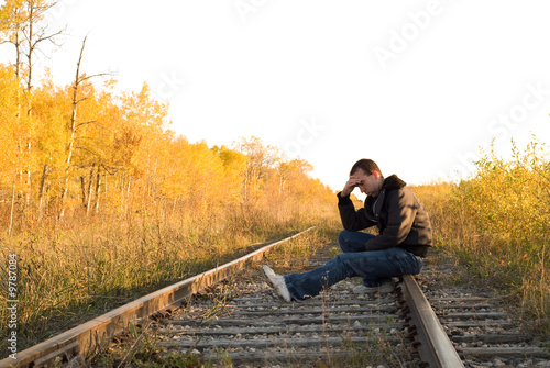 A man sitting on the railroad tracks, in a deep depression © dragon_fang